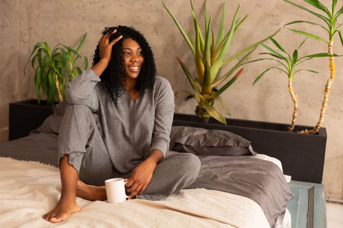 Someone sitting cross-legged on a bed in a grey melange lounge set, holding a mug